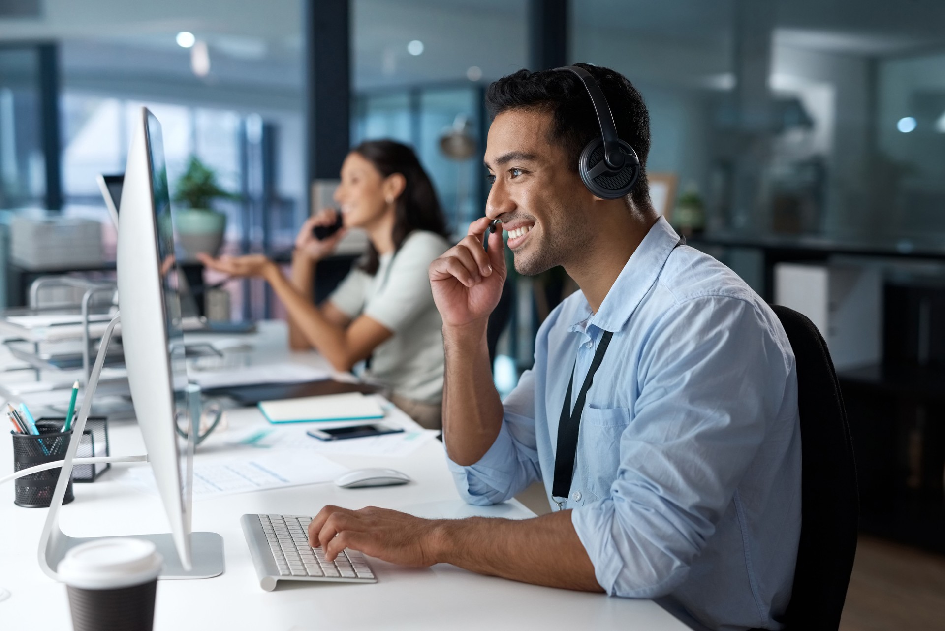 Shot of a young man using a headset and computer in a modern office